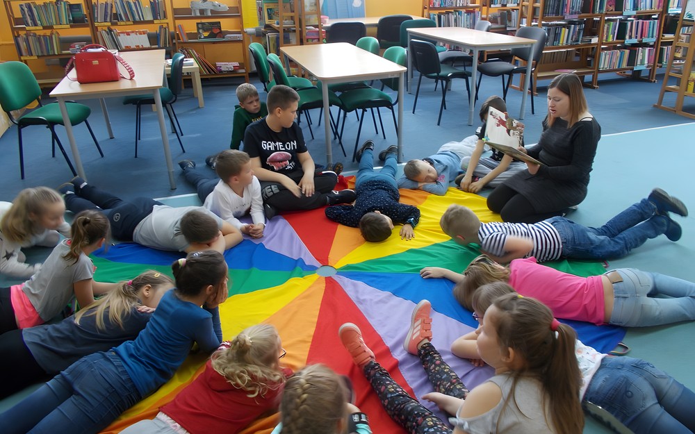 dzieci siedzą na chuście animacyjnej i słuchają bibliotekarki