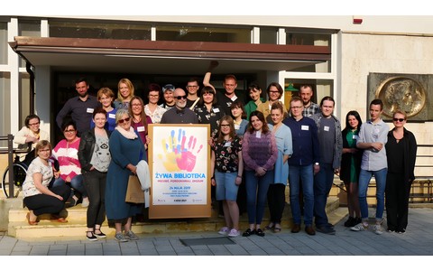 Wspólne zdjęcie organizatorów Żywej Biblioteki 2019. Pośrodku uczestników widnieje plakat promujący to wydarzenie.