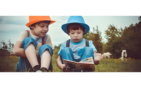 Dwaj chłopcy czytają książki na łące