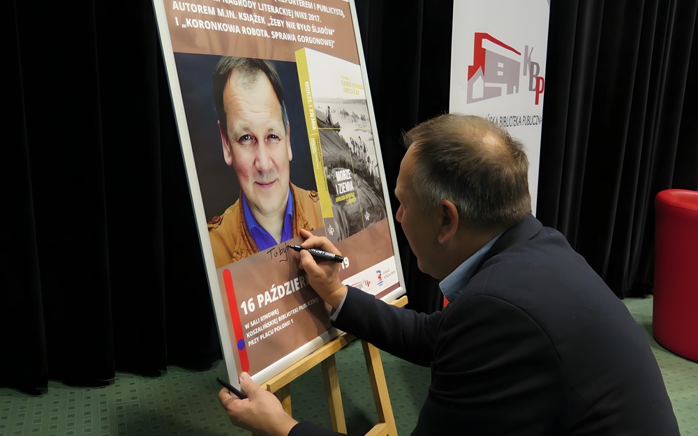 Cezary Łazarewicz składa pamiątkowy autograf na plakacie promującym spotkanie w KBP