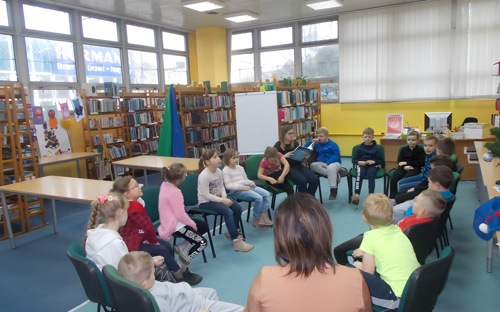 Dzieci słuchają opowiadania czytanego przez bibliotekarkę