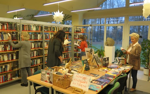 Wnętrze Koszalińskiej Biblioteki Publicznej. Na stole widoczne są nowości książkowe. Cztery bibliotekarki przeglądają zbiory biblioteczne
