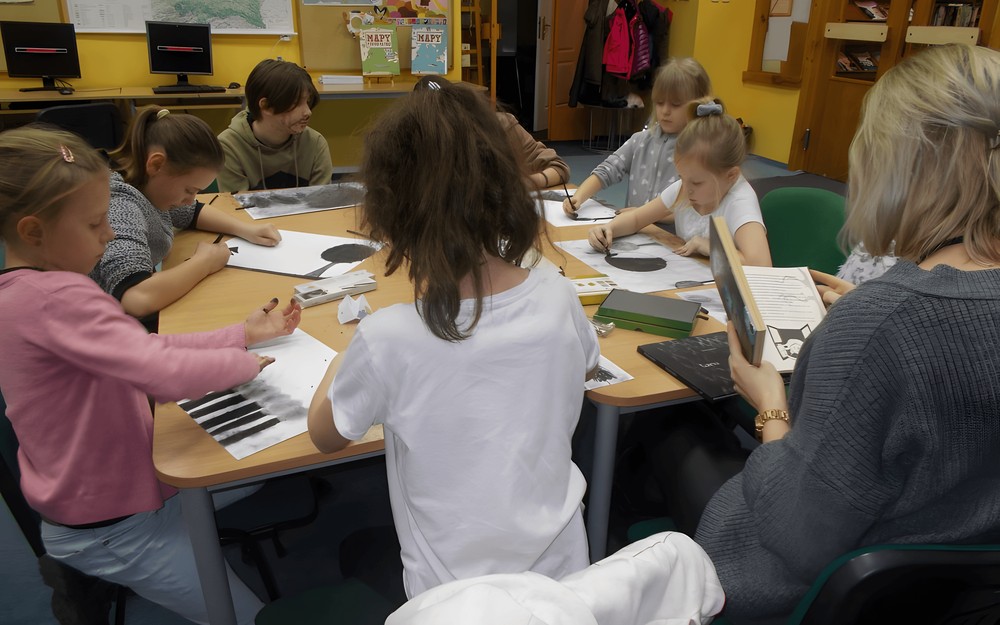 Dzieci wykonują prace plastyczne i słuchają, czytaną przez bibliotekarkę, książkę