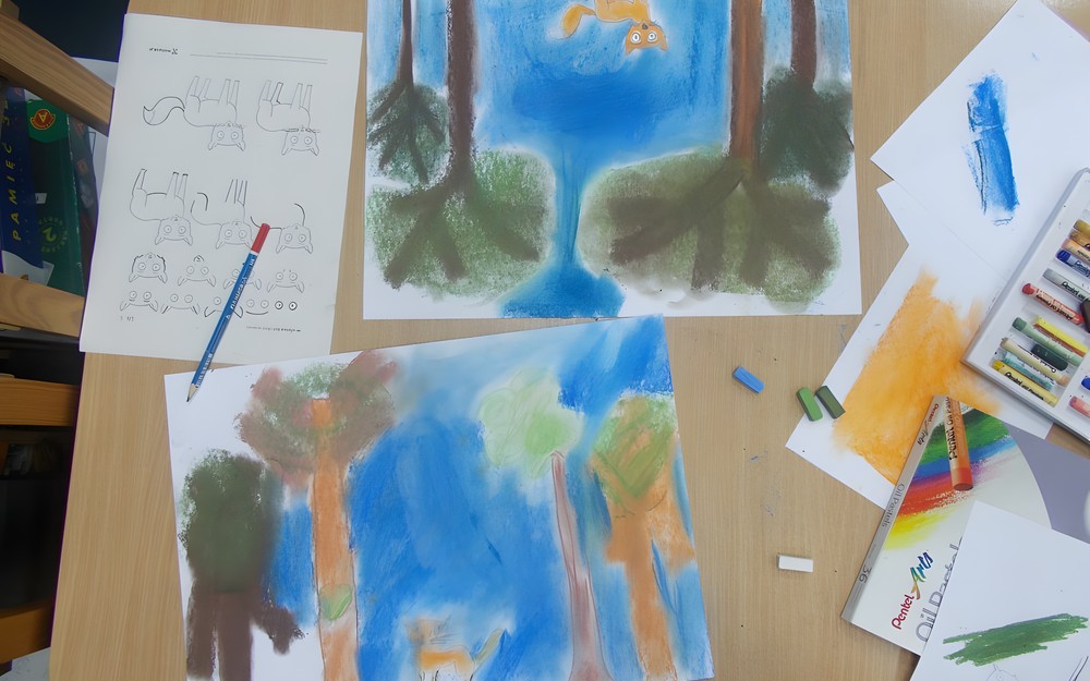 Dzieci siedzą przy stole i wykonują prace plastyczne