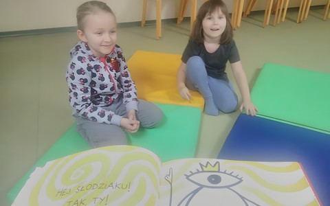 Dwie dziewczynki podczas zajęć siedzą na materacach i słychają czytanej książki