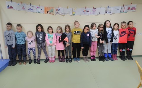 Przedszkolaki stoją pod ściana i prezentują swoje prace.