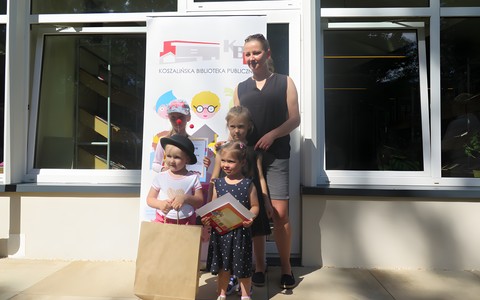 Laureaci (dzieci z Panią) powiatowego przeglądu recytatorskiego dla przedszkolaków "Wierszowanie z Agnieszką Frączek" stoją na tle dziecięcego rollupu, na tarasie Koszalińskiej Biblioteki Publicznej