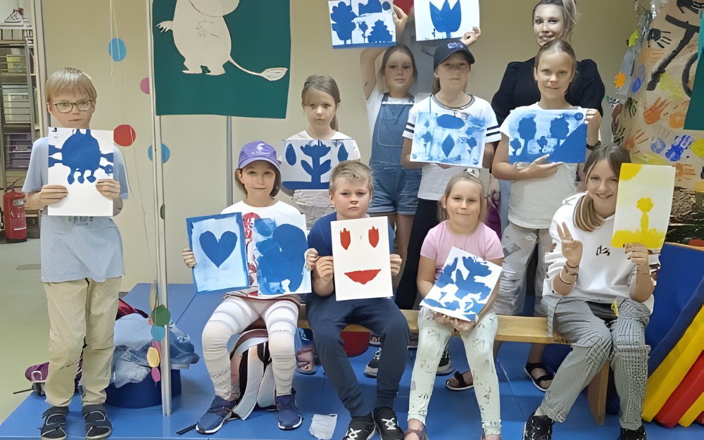 Prowadząca i uczestnicy warsztatów prezentują swoje prace plastyczne.