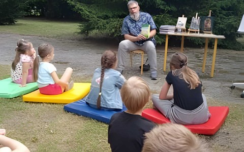 Spotkanie autorskie w ogrodzie Filii nr 9 KBP. Pawł Wakuła, autor książek dla dzieci rozmawia z uczestnikami Bezpiecznych Wakacji.