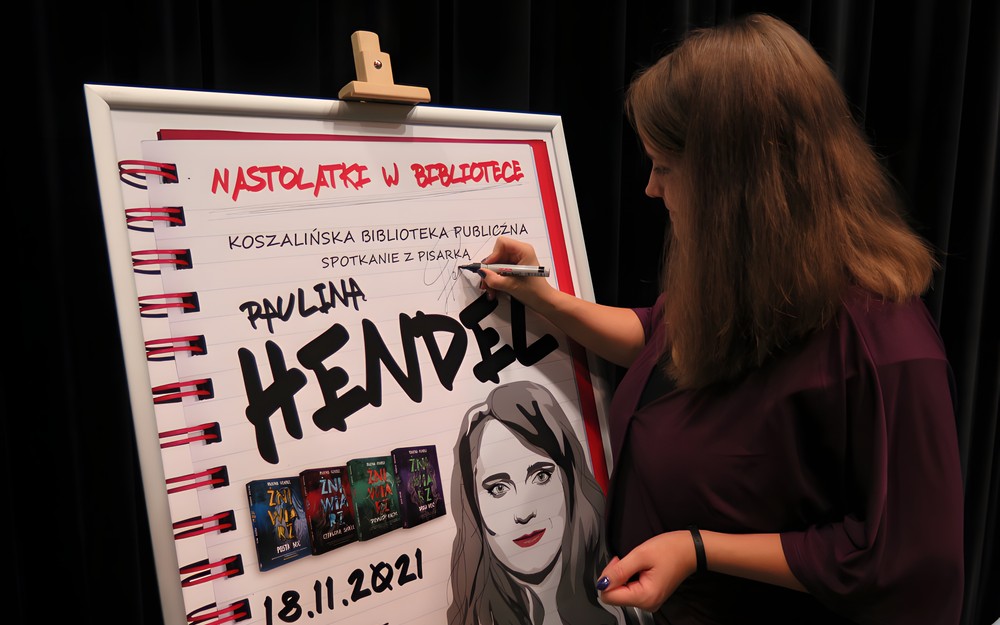 Paulina Hendel podpisuje plakat ze spotkania autorskiego.