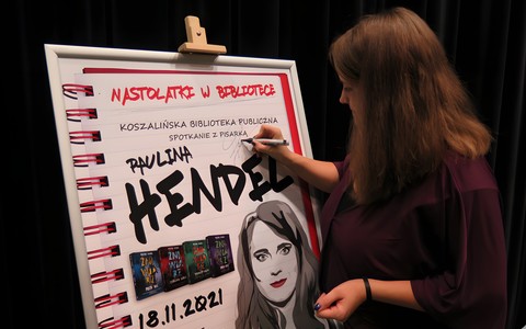 Paulina Hendel podpisuje plakat ze spotkania autorskiego.