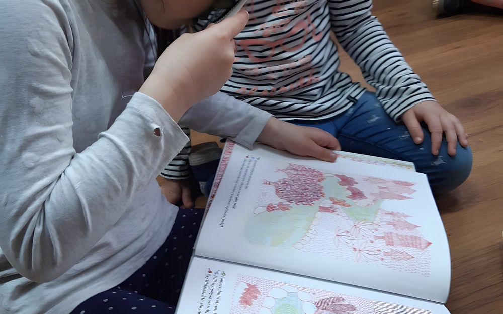 Przedszkolaki w bibliotece oglądają książki.