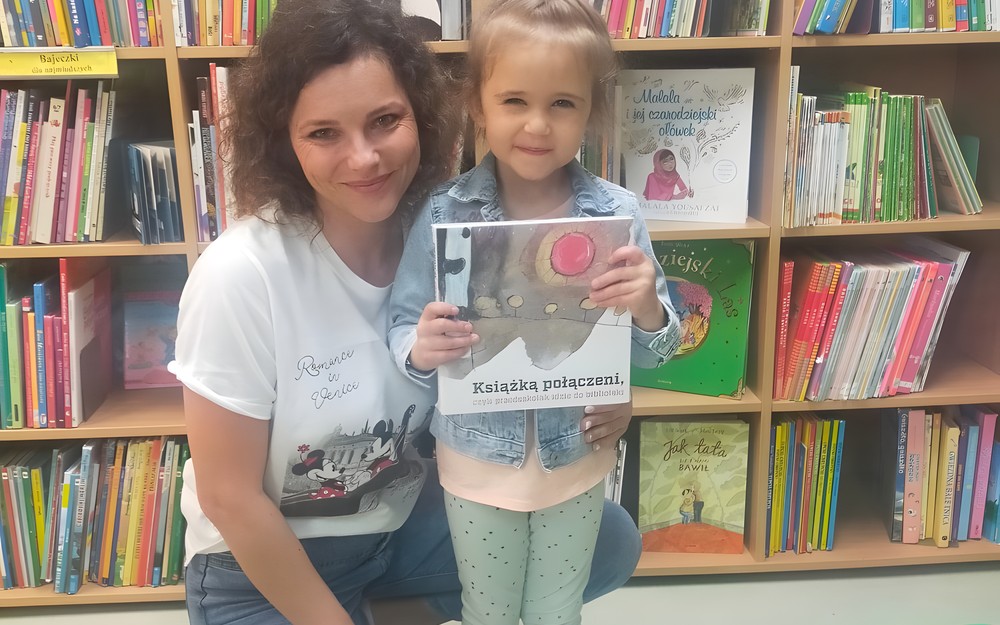 Dziewczynka z bibliotekarką prezentują książeczkę