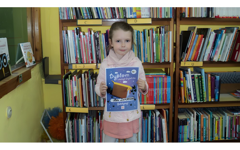 dziewczynka pozuje do zdjęcia z dyplomem "Mała książka, wielki człowiek"
