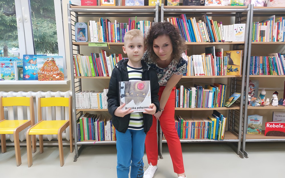 Chłopiec pozuje z książeczką i bibliotekarką