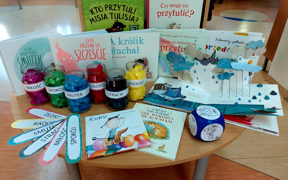 Na stoliku ustawione książki, kostka i inne przedmioty potrzebne do przeprowadzenia lekcji i emocjach