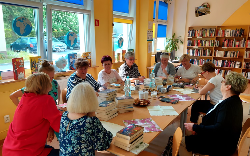 Czytelniczki siedzą przy stołach, na których rozłożone są nowości książkowe - rozpoczynamy spotkanie