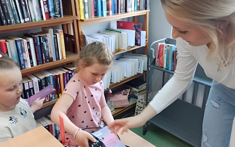 Dziecko, z pomocą bibliotekarki, skanuje kod kreskowy z książki