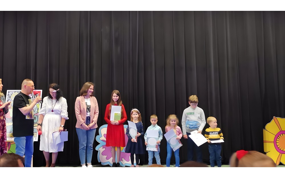 Dzieci wraz z bibliotekarką stoją na scenie i prezentują nagrody
