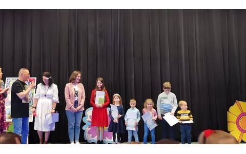 Dzieci wraz z bibliotekarką stoją na scenie i prezentują nagrody