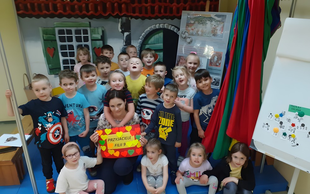 Dzieci z biblotekarką pozują z plakatem przyjaźni.