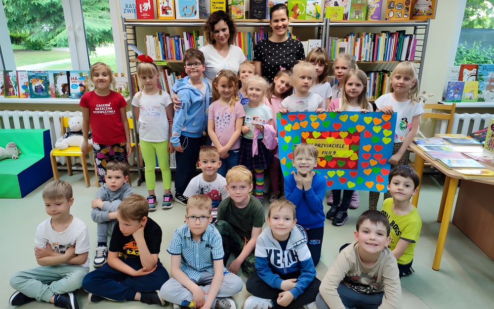 Bibliotekarki i dzieci pozują z plakatem przyjaźni