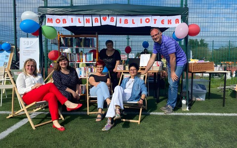 Zdjęcie przedstawia bibliotekarzy Martę, Sylwię, Dorotę, Anię, Małgorzatę i Piotra na stoisku mobilnej biblioteki.