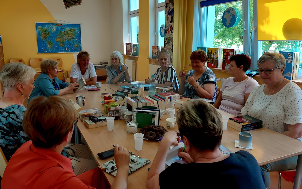 Panie siedzą przy stole, na którym rozłożone są nowości wydawnicze i recenzują przeczytane książki