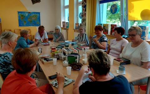 Panie siedzą przy stole, na którym rozłożone są nowości wydawnicze i recenzują przeczytane książki