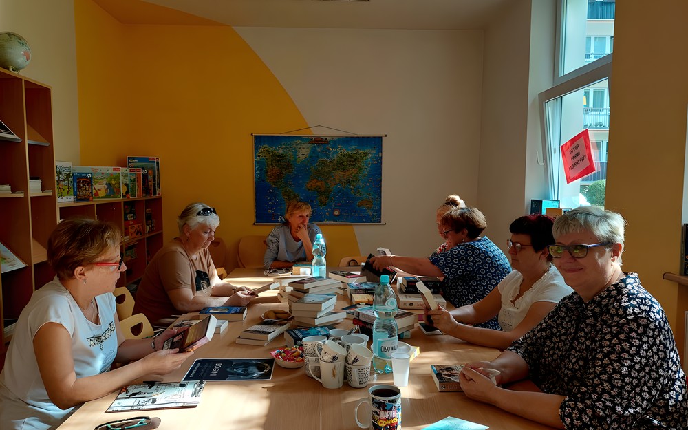 Spotkanie COOLturalnych 6 przy stołach zasypanych książkowymi nowościami