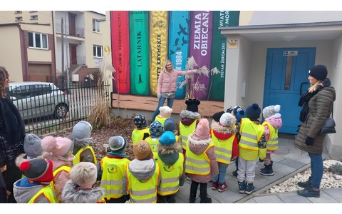 Dzieci stoją przd biblioteką słuchając bibliotekarki