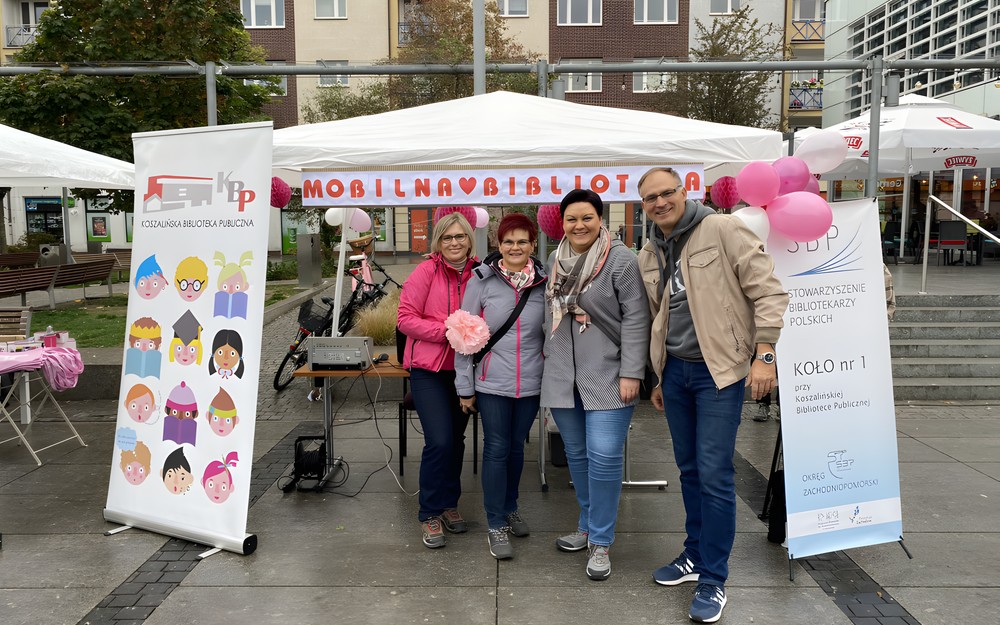 Bibliotekarze należący do SBP Koła w Koszalinie, stoją na tle stoiska Mobilnej Biblioteki