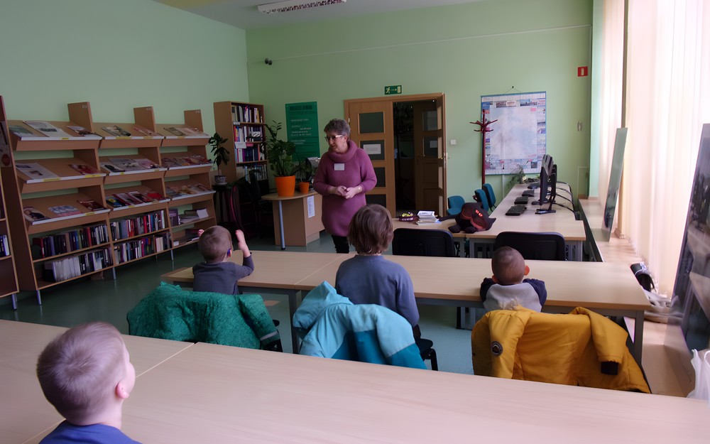 na zdjęciu dzieci słuchają co mówi bibliotekarka