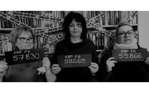 Na zdjęciu Gosia, Wiola i Ewa stoją na tle regałów z kryminałami, trzymając tabliczki z numerami inwentarzowymi popularnych kryminałów