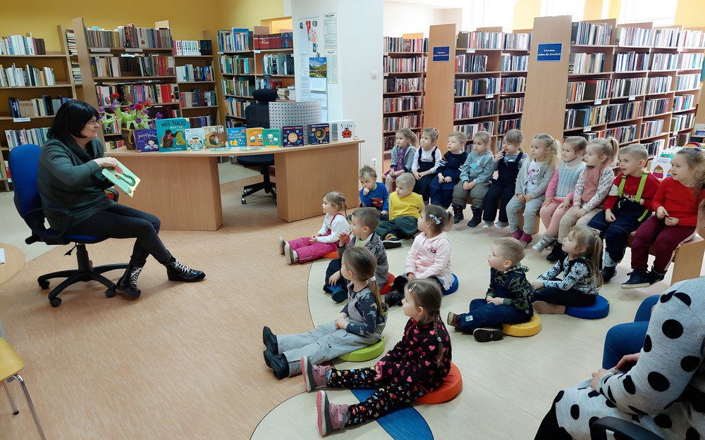 Na zdjęciu Wiola prezentuje dzieciom siędzącym na podłodze, książkę pt. Wszyscy ziewają