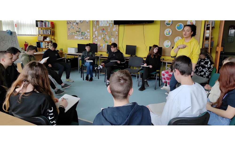 dzieci siedzą na krześle, a bibliotekarka wyjasnia im reguły gry