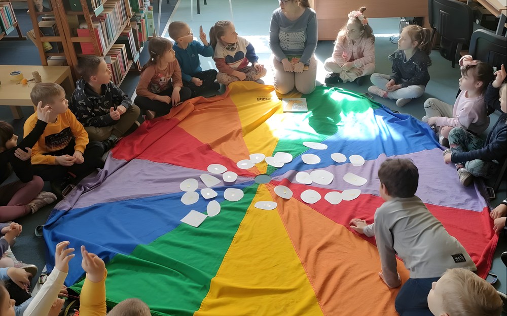 bibliotekarka czya dzieciom siedzącym na chuście książkę
