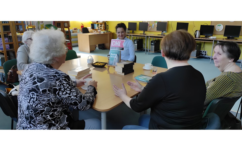panie wraz z bibliotekarką dyskutują o książce siedząc przy stole