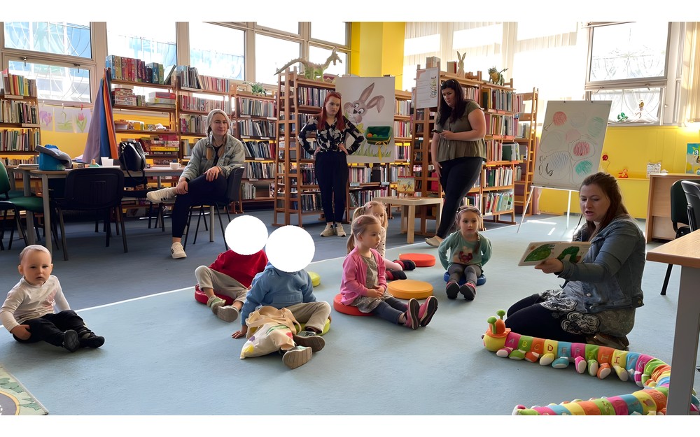 Głośne czytanie książki dzieciom siedzącym na pufkach