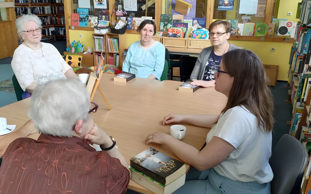 uczestniczki dkk wraz z bibliotekarką siedzą przy stole i dyskutują o książce