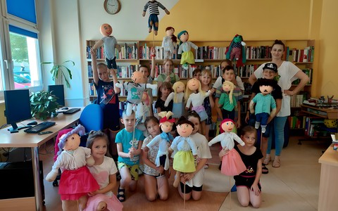 Uczestnicy warsztatów lalkarskich pozują do grupowego zdjęcia z wykonanymi przez siebie kukiełkami i prowadzącą - panią Ewą