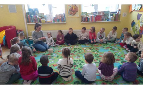 Przedszkolaki siedzą w kole na dywanie, a bibliotekarka czyta zagadkę