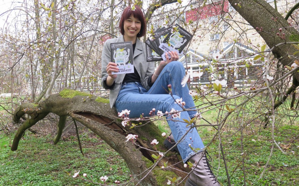 Katarzyna Bielecka z Mediateki KBP prezentuje nowe wydanie KGK siedząc na konarze drzewa.
