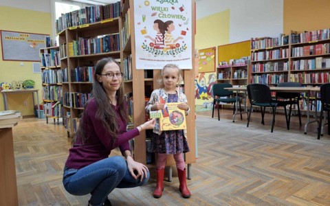 Dziewczynka wraz z bibliotekarką pokazuje nowo nabyty pakiet z akcji "Mała książka, wielki człowiek"