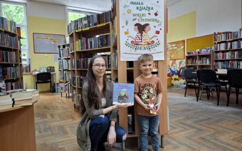 Bibliotekarka wraz z dzieckiem, nowym czytelnikiem, pokazują książkę, karte oraz zakładkę projektu "Mała książka- wielki człowiek"