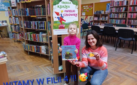 Dziewczynka wraz z bibliotekarkami pokazuje książkę i zakładkę
