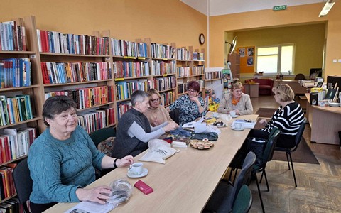 Panie siedzą przy stole, robią na drutach i rozmawiają