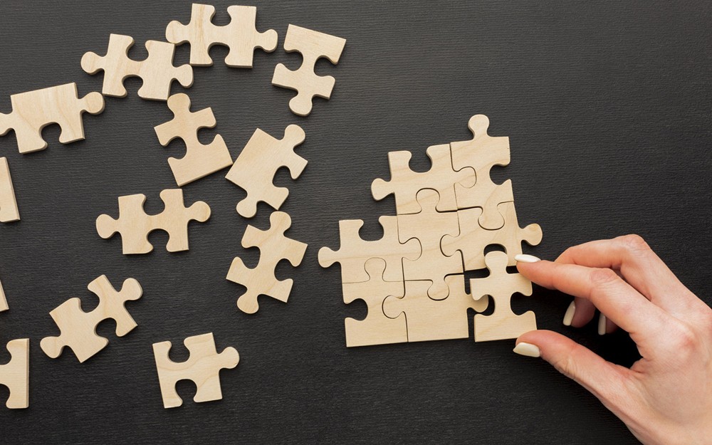 Zdjęcie przedstawia rozsypane puzzle i rękę trzymającą element układanki. (fot. Freepik)