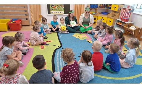 bibliotekarka z mamą Mikolaja czytają dzieciom opowiadanie "Żabka mała" z opaskami żabek na głowie
