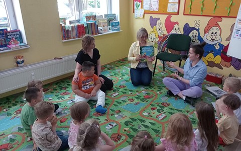 Bibliotekarka czyta dzieciom książkę, dzieci siedzą w kole
